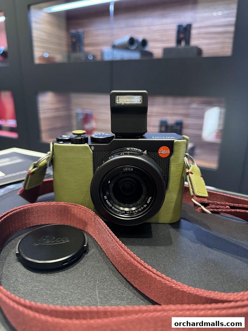 A Leica camera with a green case and red strap is displayed on a dark surface.