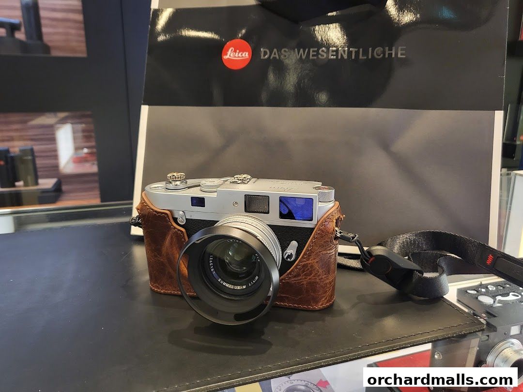 A Leica camera with a leather case and strap is displayed on a black surface.