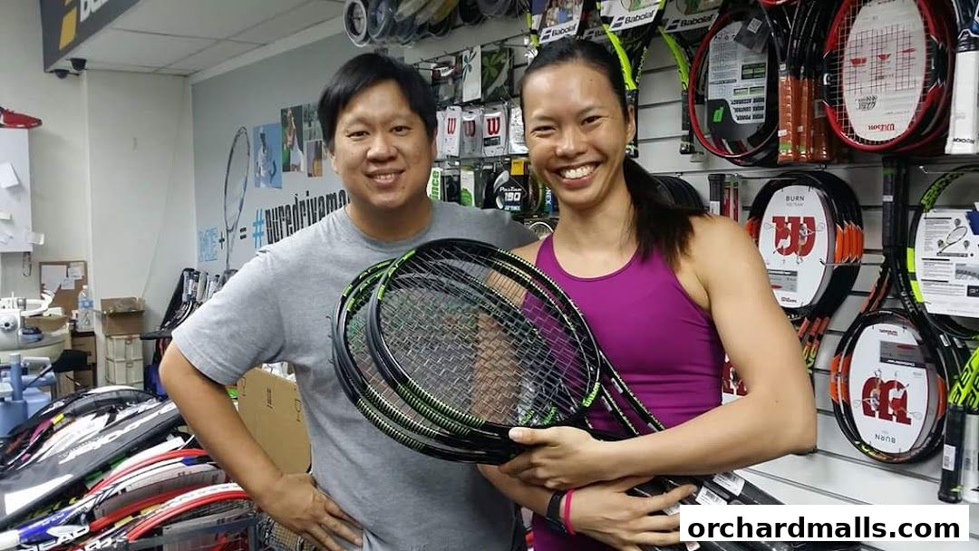Two smiling people holding tennis rackets in a sports equipment store.