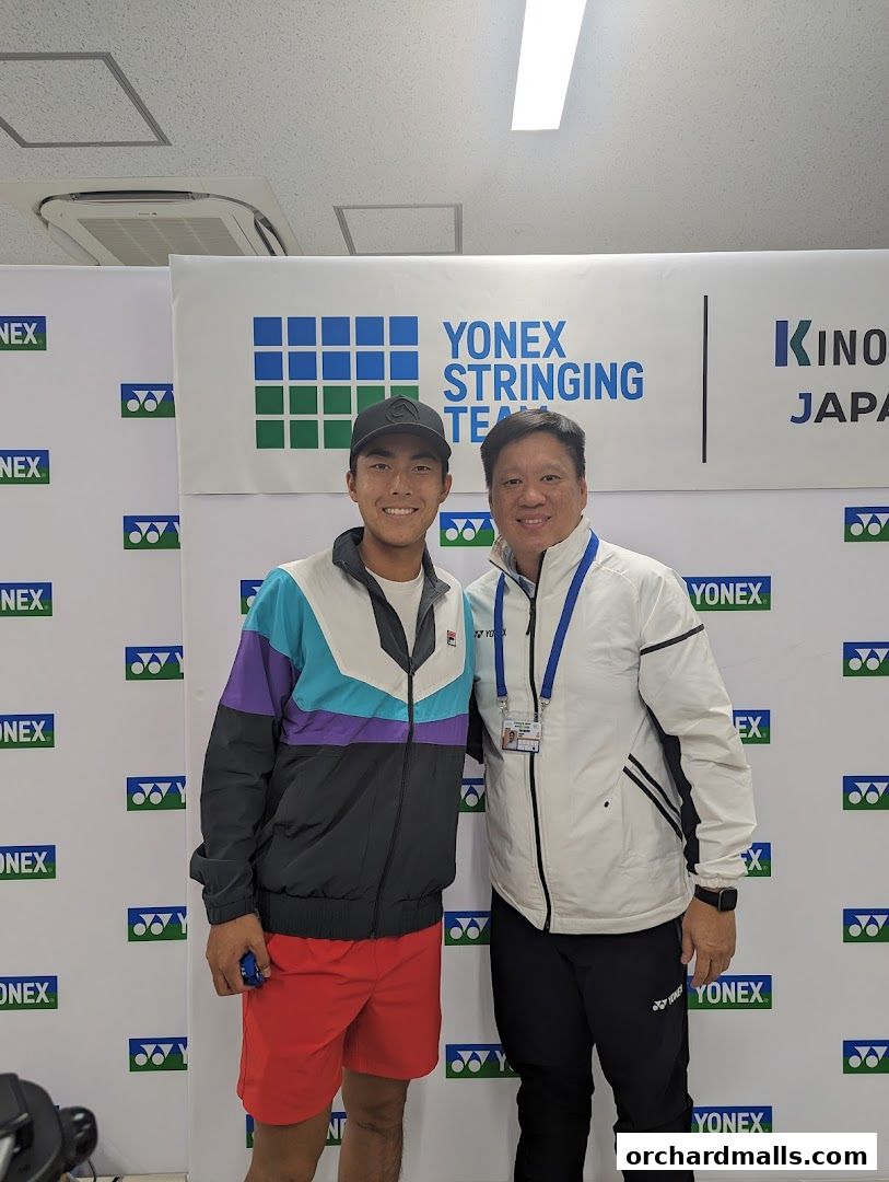 Two men pose for a photo in front of a Yonex Stringing Team banner.