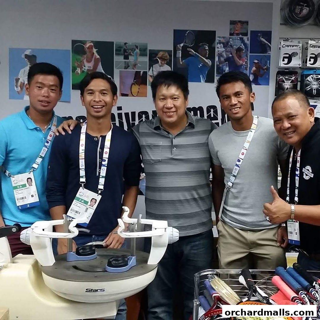 A group of men posing with a tennis stringing machine and rackets.