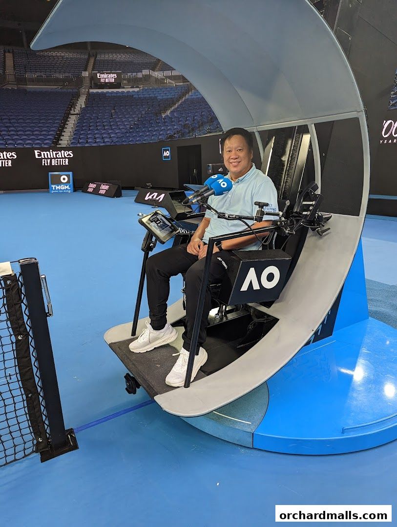A man sits in a chair on a tennis court with microphones in front of him.