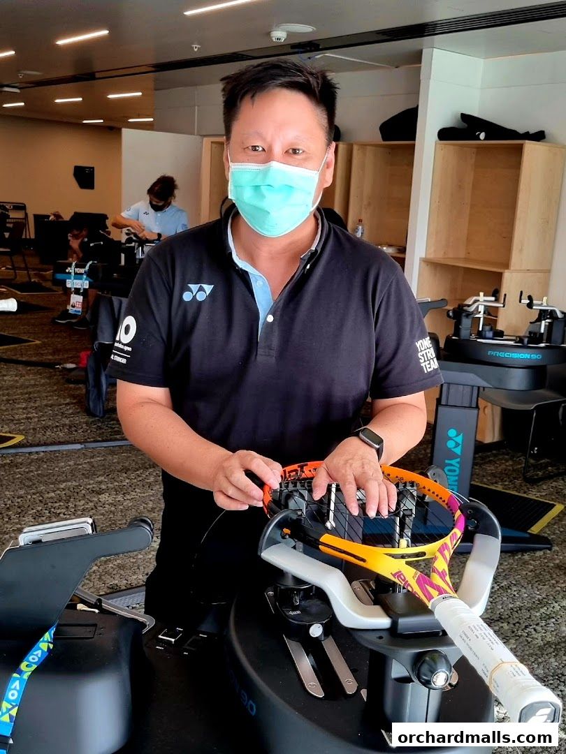 A man in a mask is stringing a tennis racket at Leisure Sports.