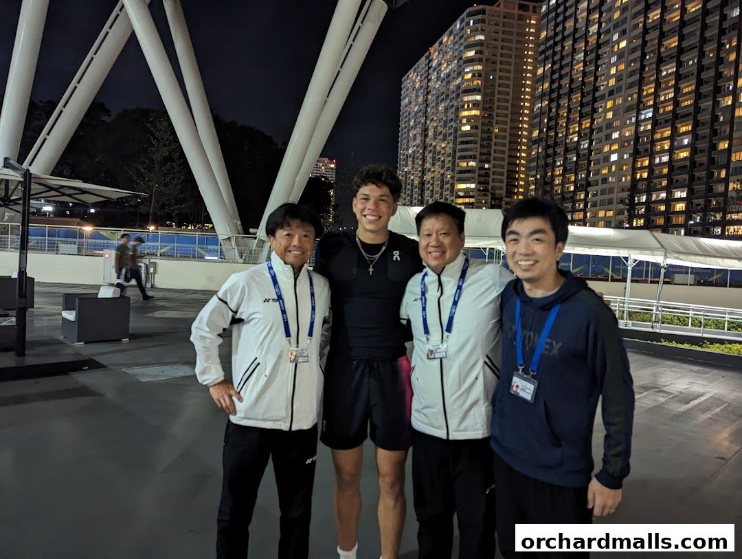 Four men in athletic wear pose for a photo outdoors at night with a city skyline in the background.
