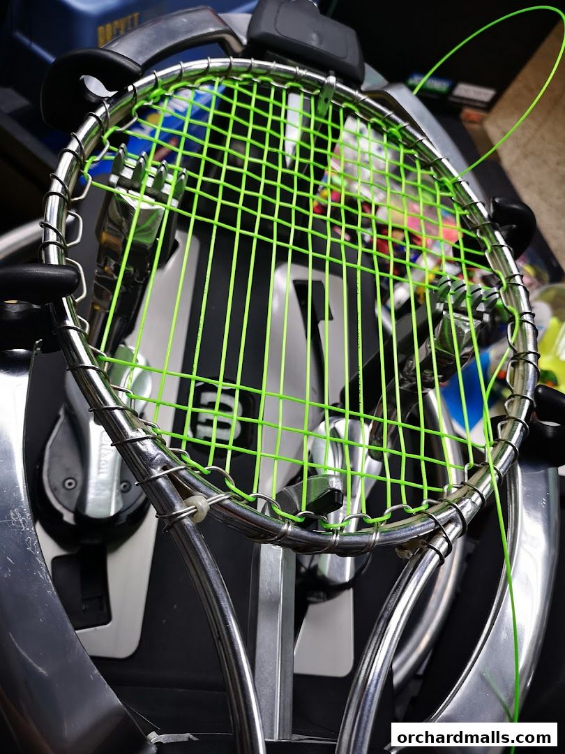 Close-up of a tennis racket being restrung with bright green strings.