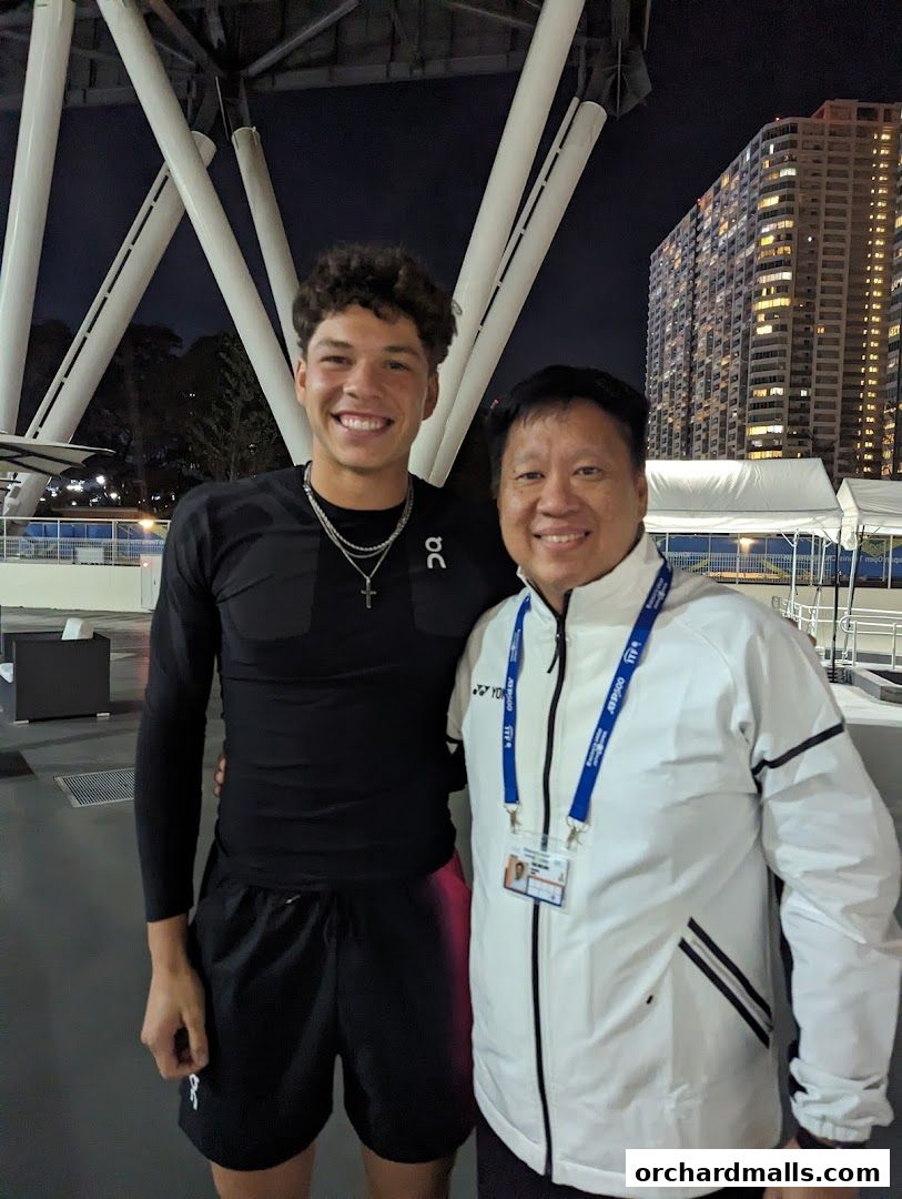 Two men smiling, one in athletic wear, the other in a white jacket.