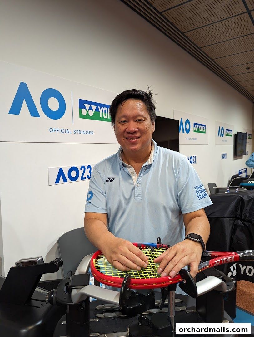 A man smiles while stringing a tennis racket at a sports event.