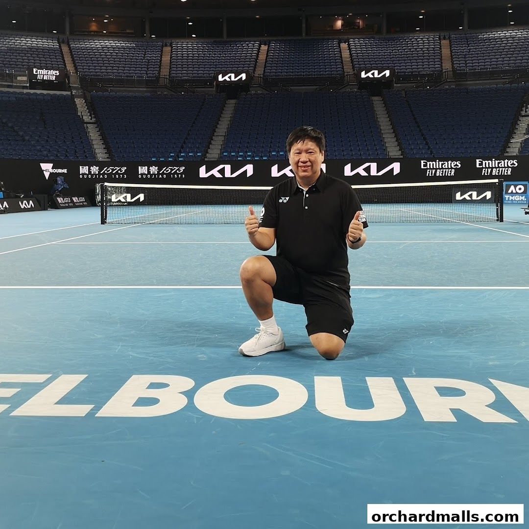 Man in sportswear posing on a tennis court with stadium seating in the background.