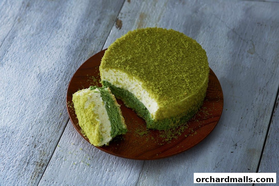 A slice of matcha cake with layers of cream and matcha sponge on a wooden plate.