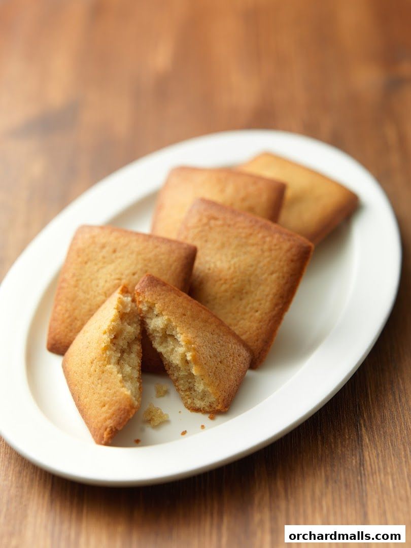 A white oval plate holds several golden-brown financiers, one broken in half.