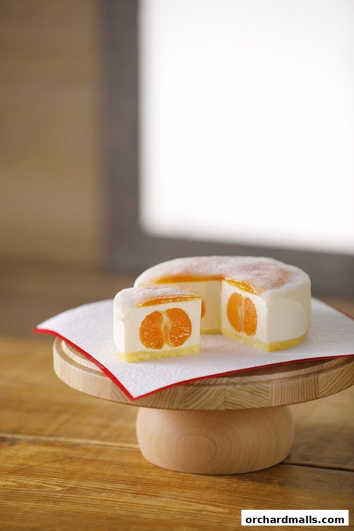 A slice of a creamy white cake with orange segments inside, presented on a wooden stand.