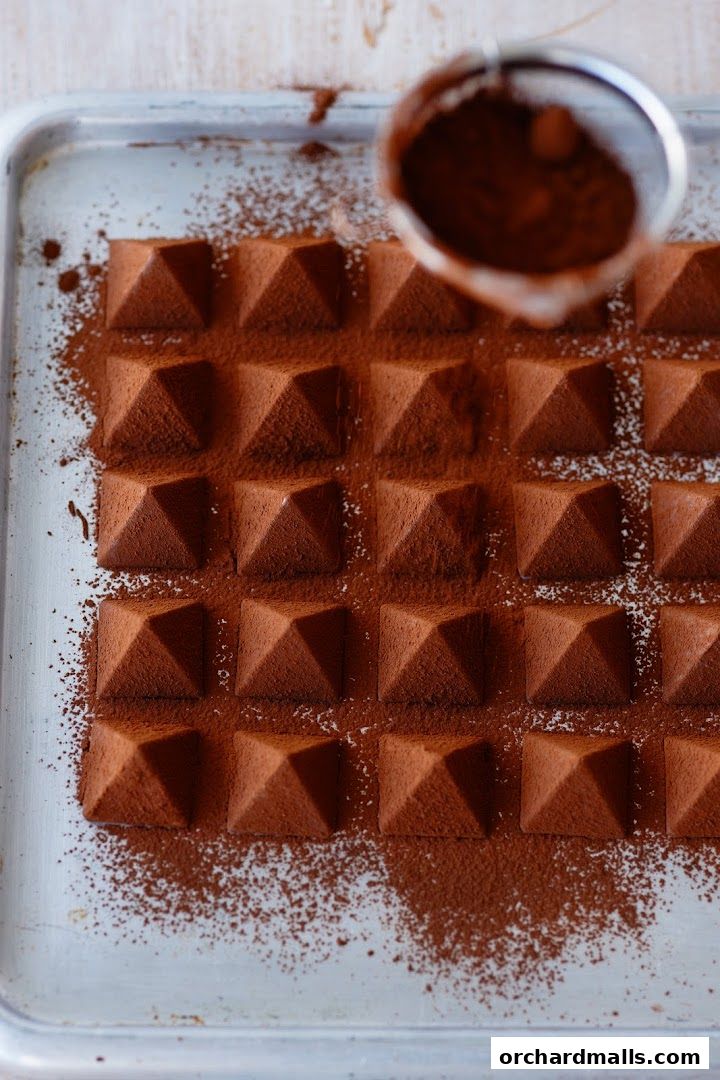 Pyramid-shaped chocolates dusted with cocoa powder on a baking tray.