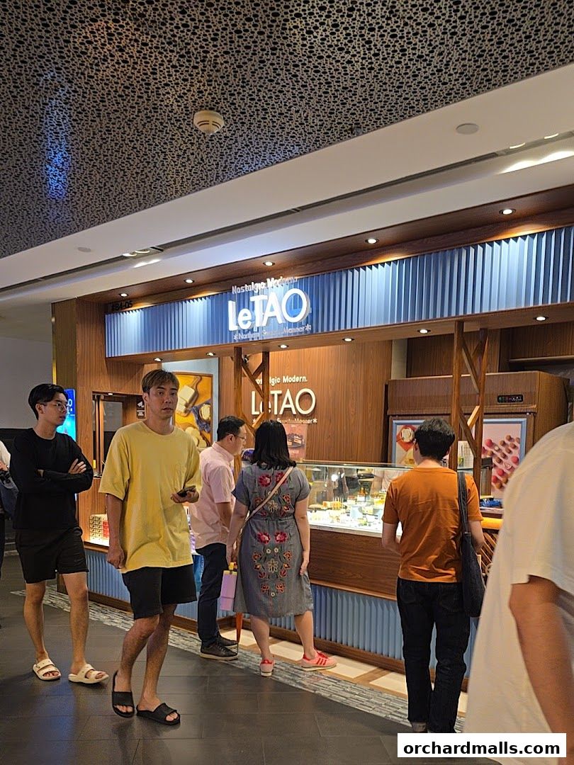 People queuing outside a LeTAO shop with a display of desserts.