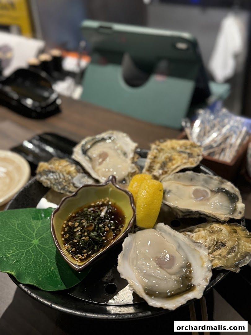 A platter of fresh oysters served with dipping sauce and lemon.