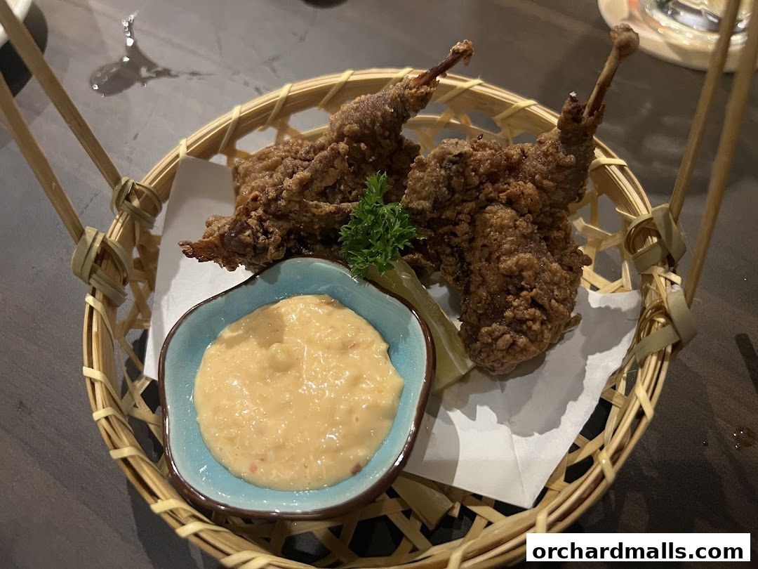 Crispy fried quail served in a basket with dipping sauce and a lemon wedge.