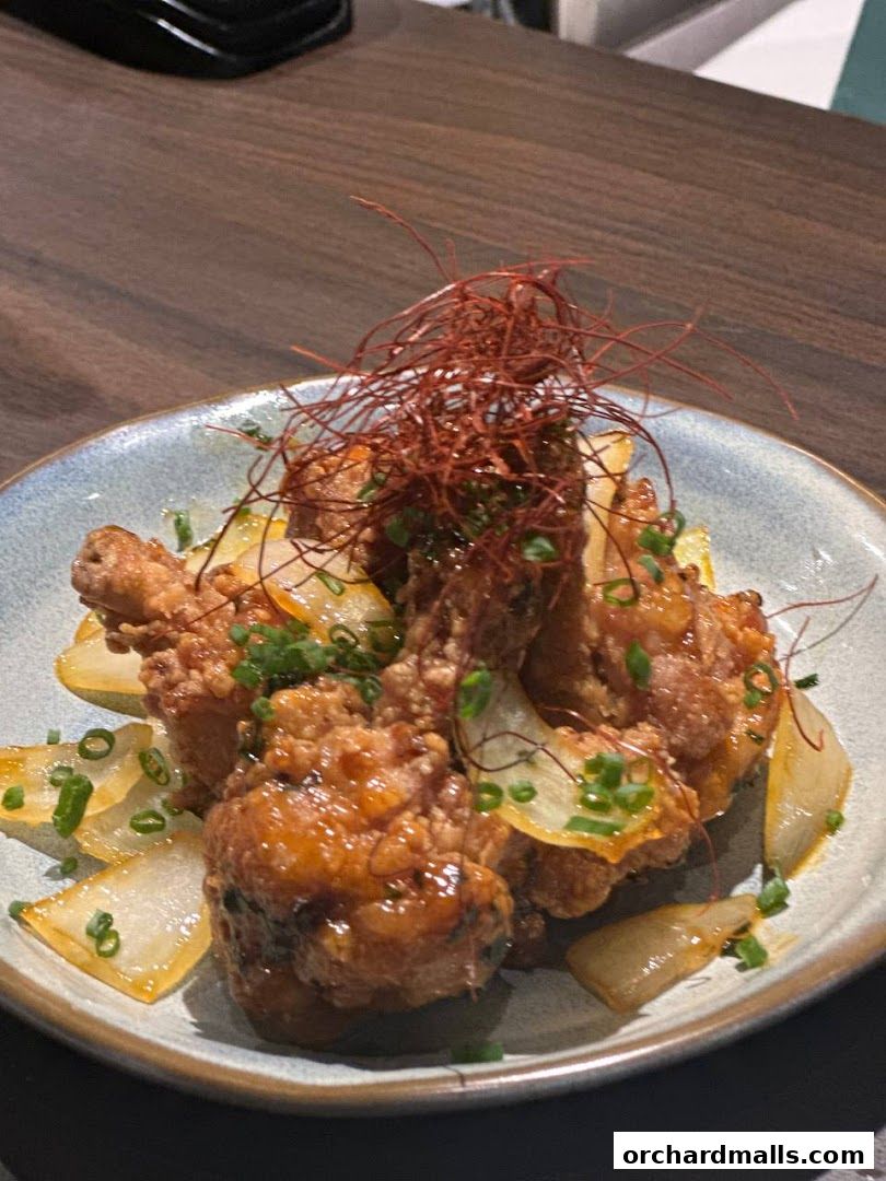 A plate of crispy fried chicken wings glazed with a sweet and savory sauce, garnished with chili threads and scallions.