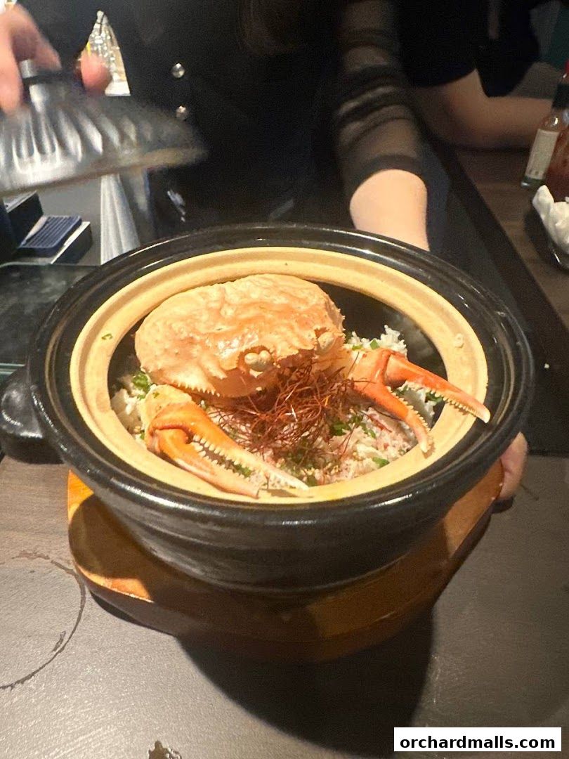 A steaming crab dish served in a pot with rice and garnished with chili threads.