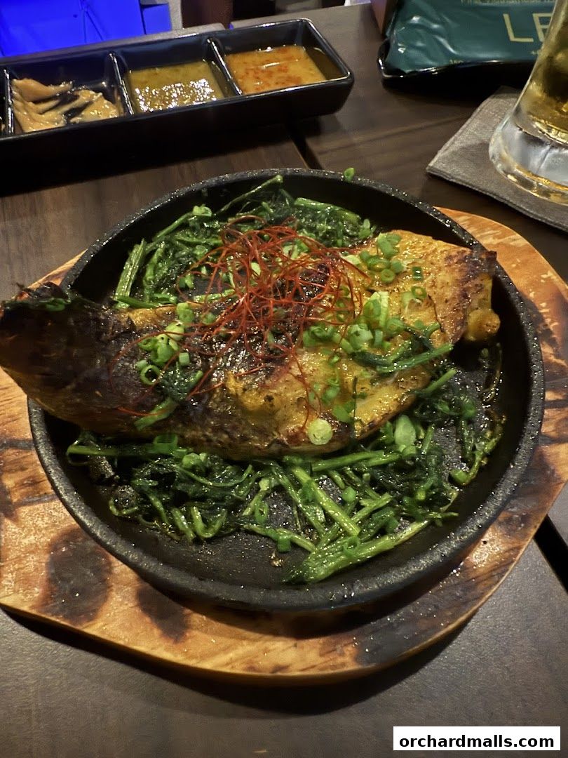 A grilled fish dish served on a sizzling plate with greens and chili threads.