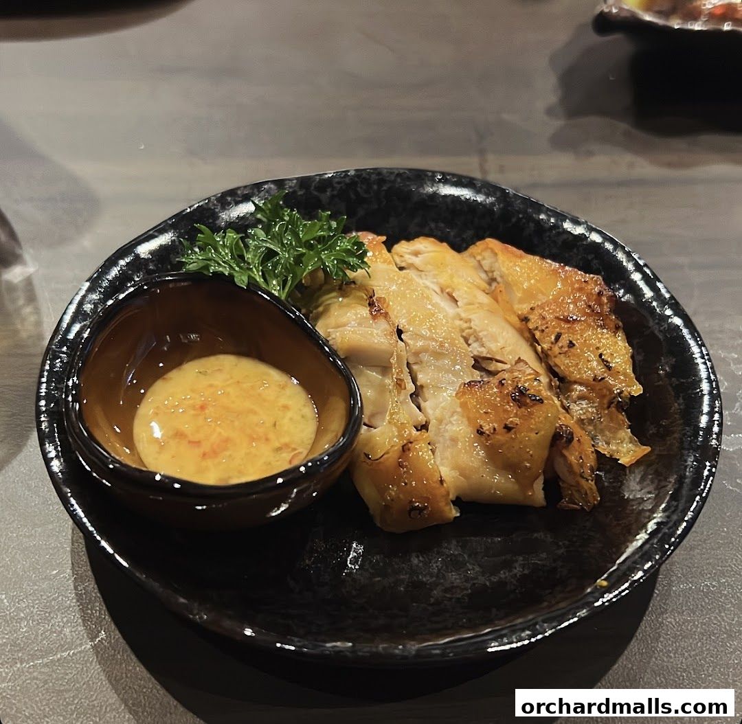 A plate of sliced grilled chicken with a side of dipping sauce and parsley.