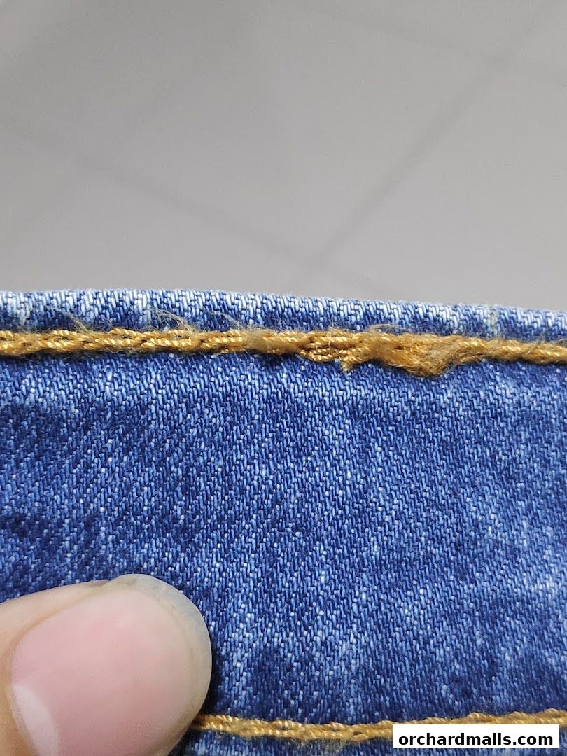 Close-up of blue denim fabric with visible stitching and a thumb.