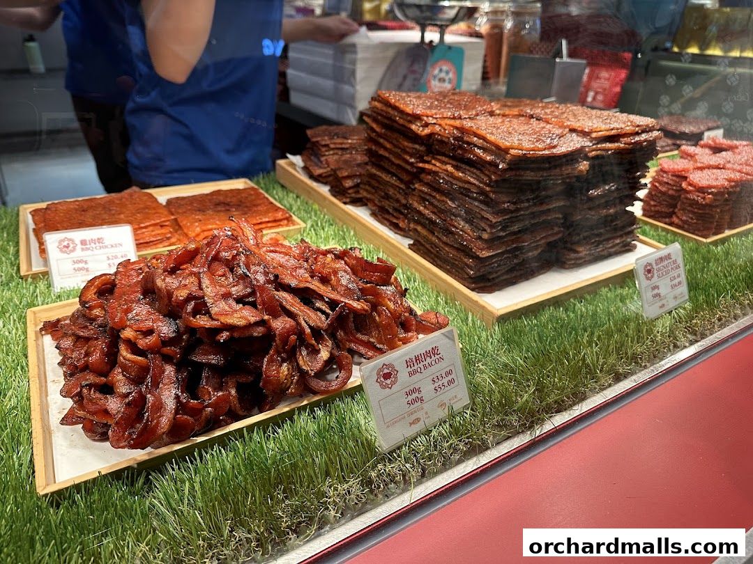 A display of various types of bak kwa, including BBQ chicken and pork, presented on artificial grass.