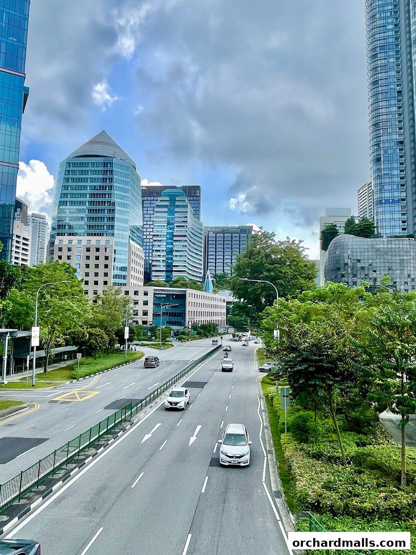 A view of a city street with cars and modern buildings under a cloudy sky.