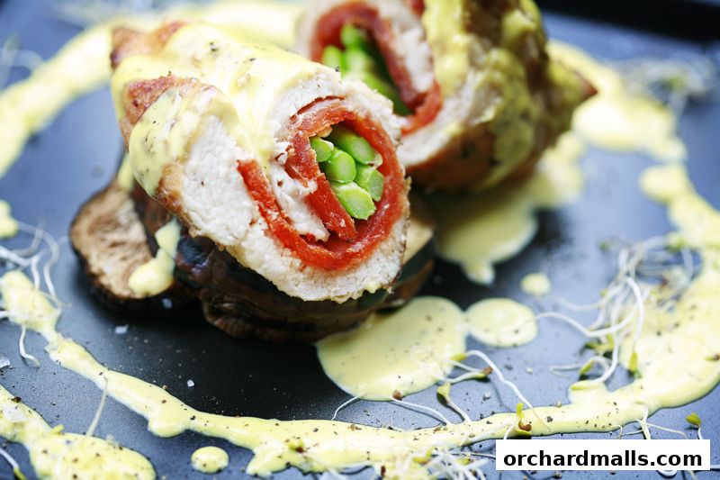 A close-up of a gourmet dish featuring rolled chicken with red pepper and asparagus, drizzled with sauce.