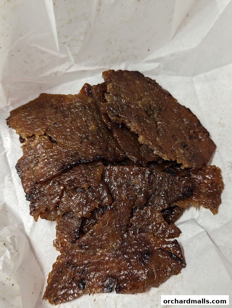A close-up shot of thinly sliced, glistening beef jerky on white paper.