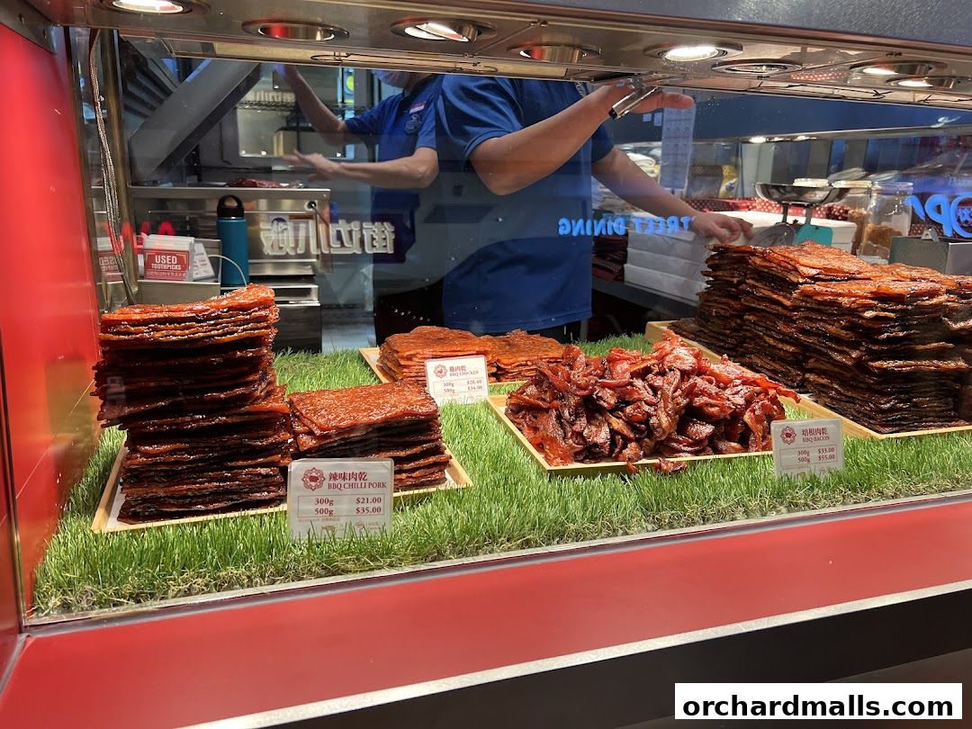 A display of stacked and loose bak kwa (dried meat) products in a shop window.