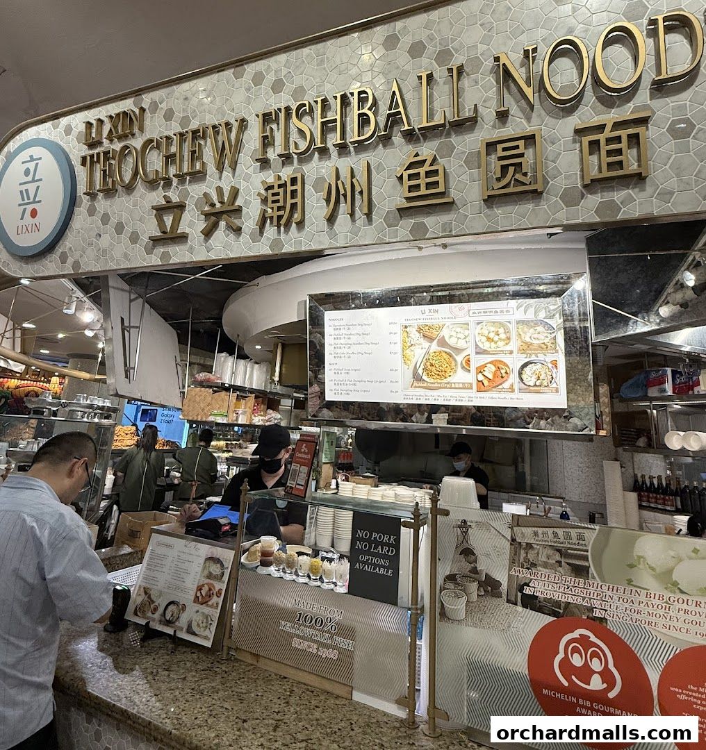 A busy noodle shop counter with staff serving customers and a menu displayed.
