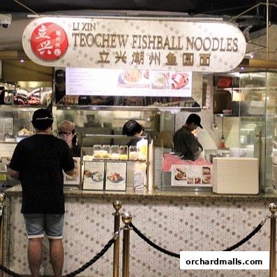 A customer stands at the counter of Li Xin Teochew Fishball Noodles, with staff preparing food.