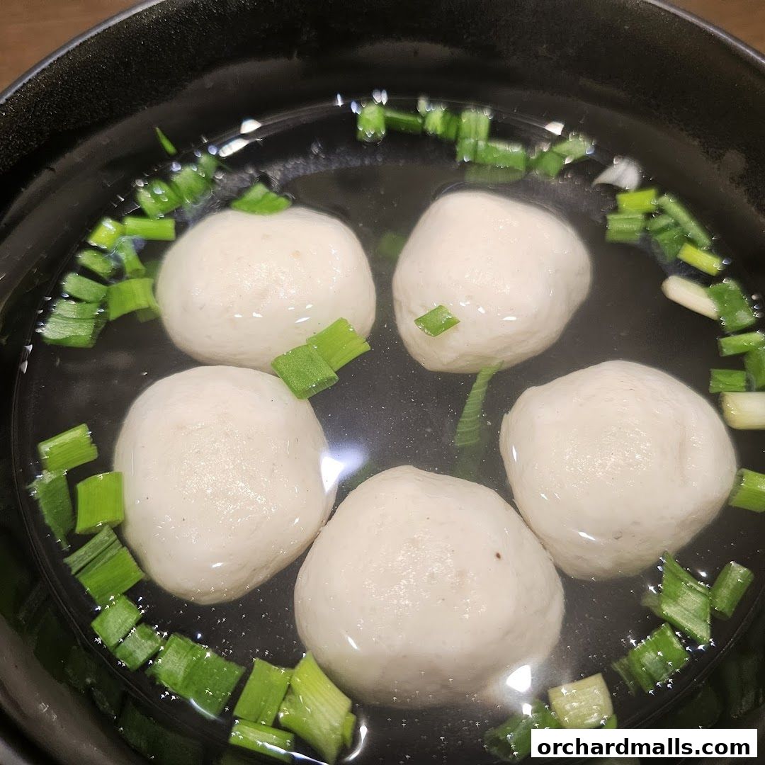A close-up shot of Teochew fishballs in a clear broth with chopped scallions.