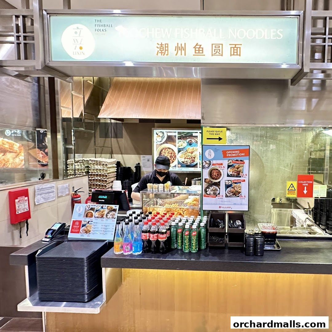 A food stall counter with a sign for Teochew Fishball Noodles and a promotional poster.