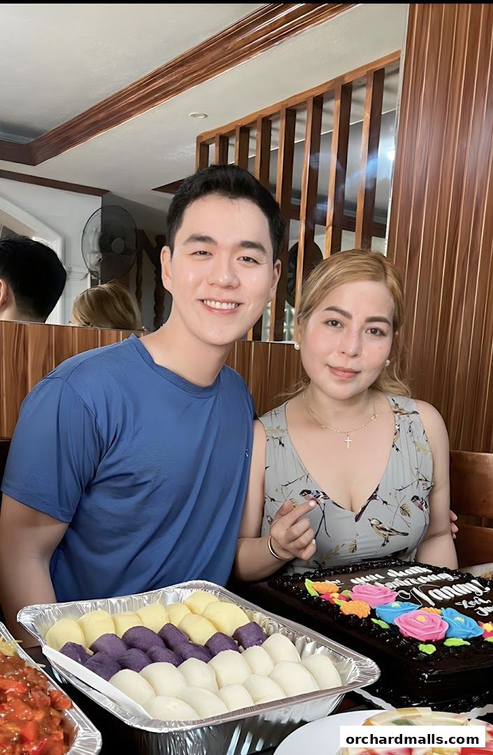 A smiling couple poses with a cake and a tray of food, possibly celebrating an event.