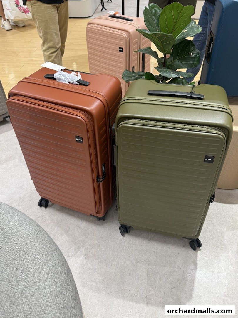 Two stylish LOJEL suitcases, one brown and one green, displayed in a retail store.