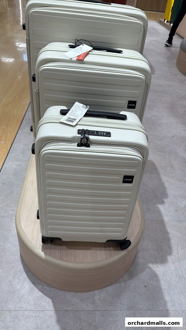 Three cream-colored LOJEL suitcases are displayed on a wooden stand.