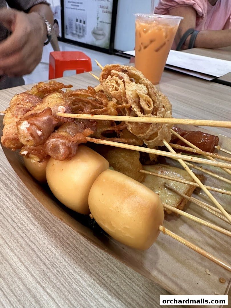 A close-up of various fried skewers and a Thai iced tea.