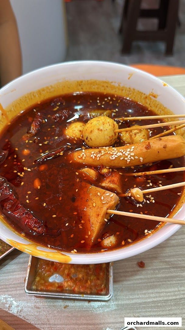 A bowl of spicy mala tang with various ingredients on skewers.