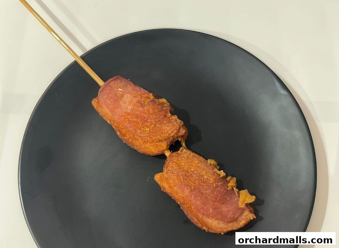 A skewer with two pieces of fried meat on a black plate.