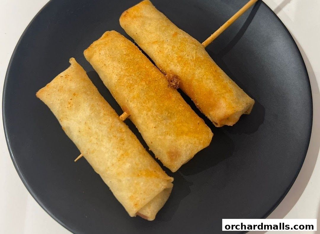 Three golden-brown spring rolls on a black plate, skewered with wooden sticks.