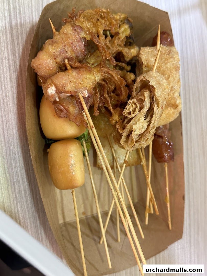 A close-up of various fried skewers in a paper tray, ready to eat.