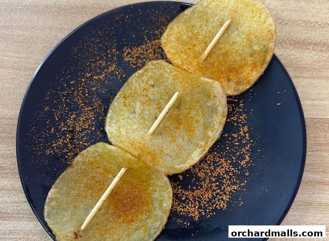 Three crispy potato slices on a stick, seasoned with spices, served on a black plate.