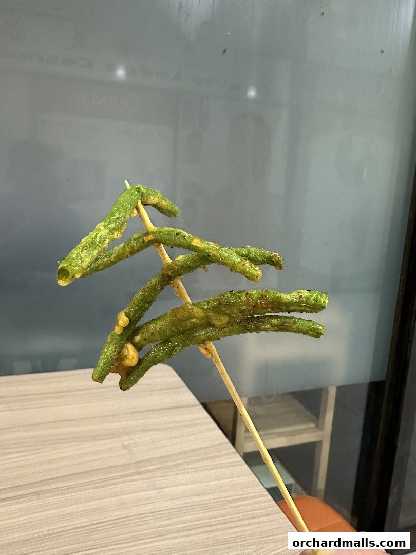 A skewer of deep-fried green beans with a crispy coating.