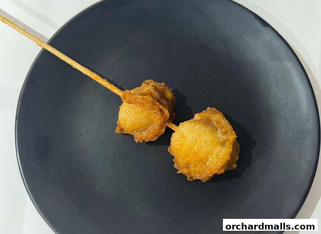 Two pieces of fried food on a skewer on a black plate.