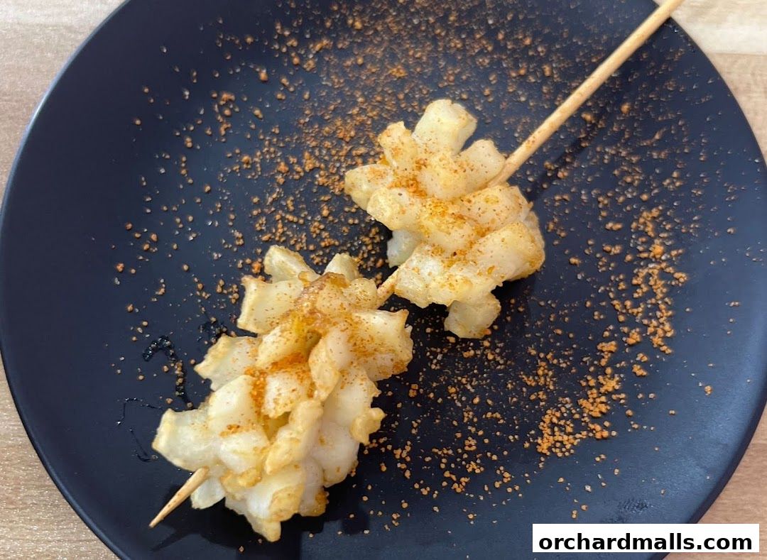 Two skewers of fried calamari, seasoned with spices, on a black plate.