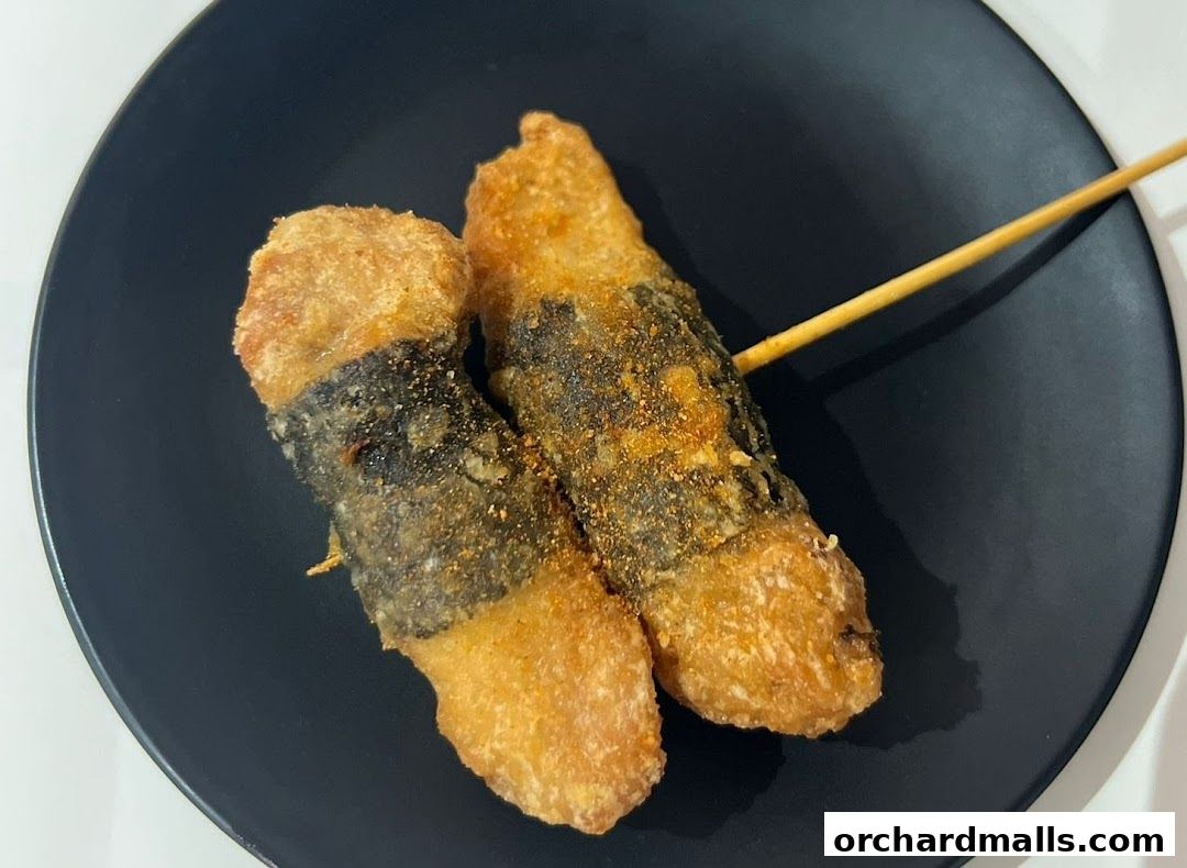 Two deep-fried snacks wrapped in seaweed on a black plate with a skewer.