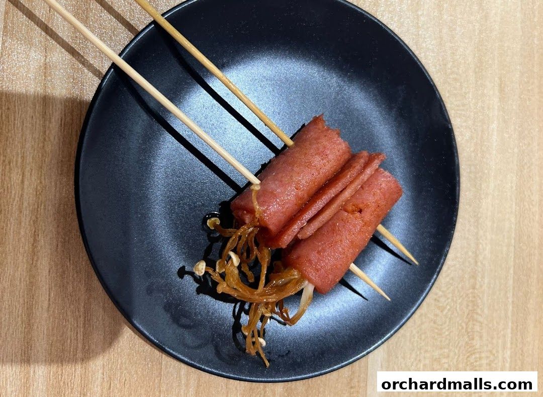 Two skewers with rolled ham and enoki mushrooms on a black plate.