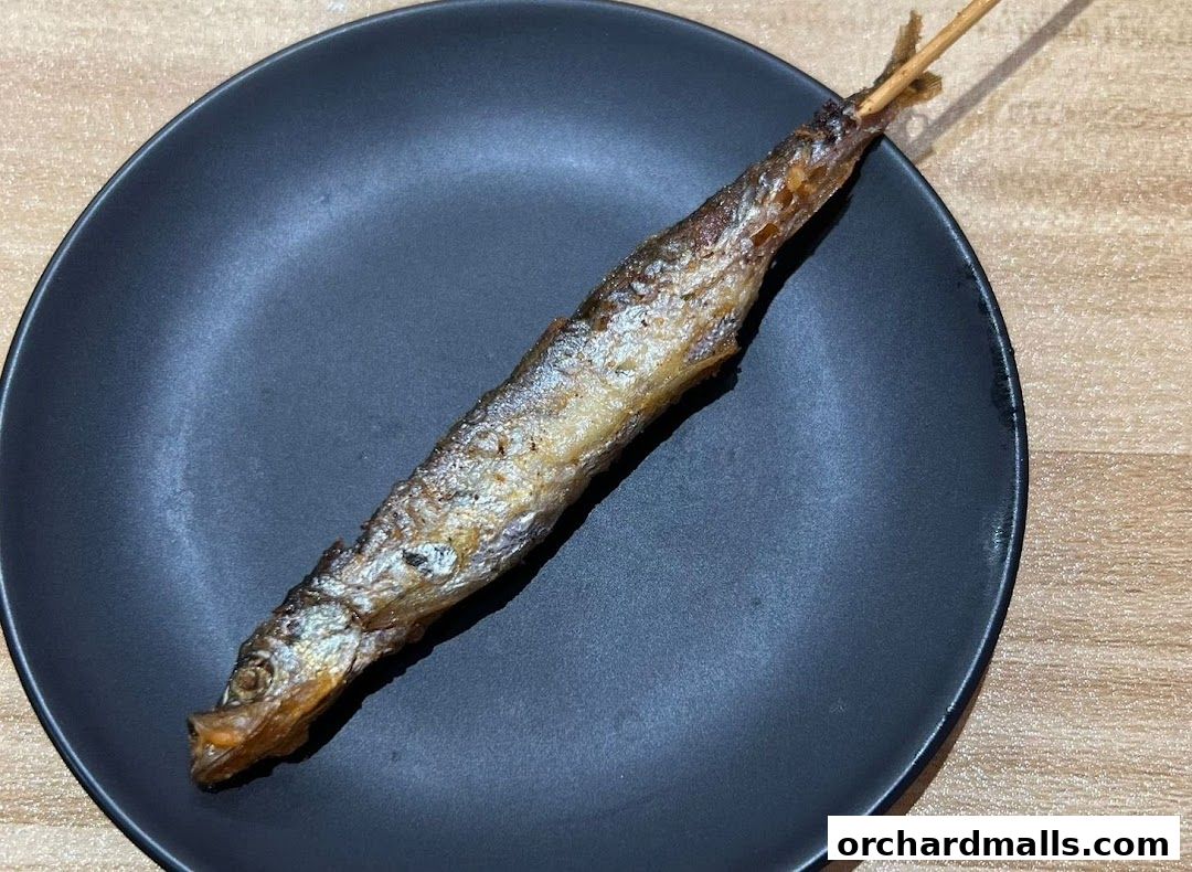 A single grilled fish on a skewer served on a black plate.