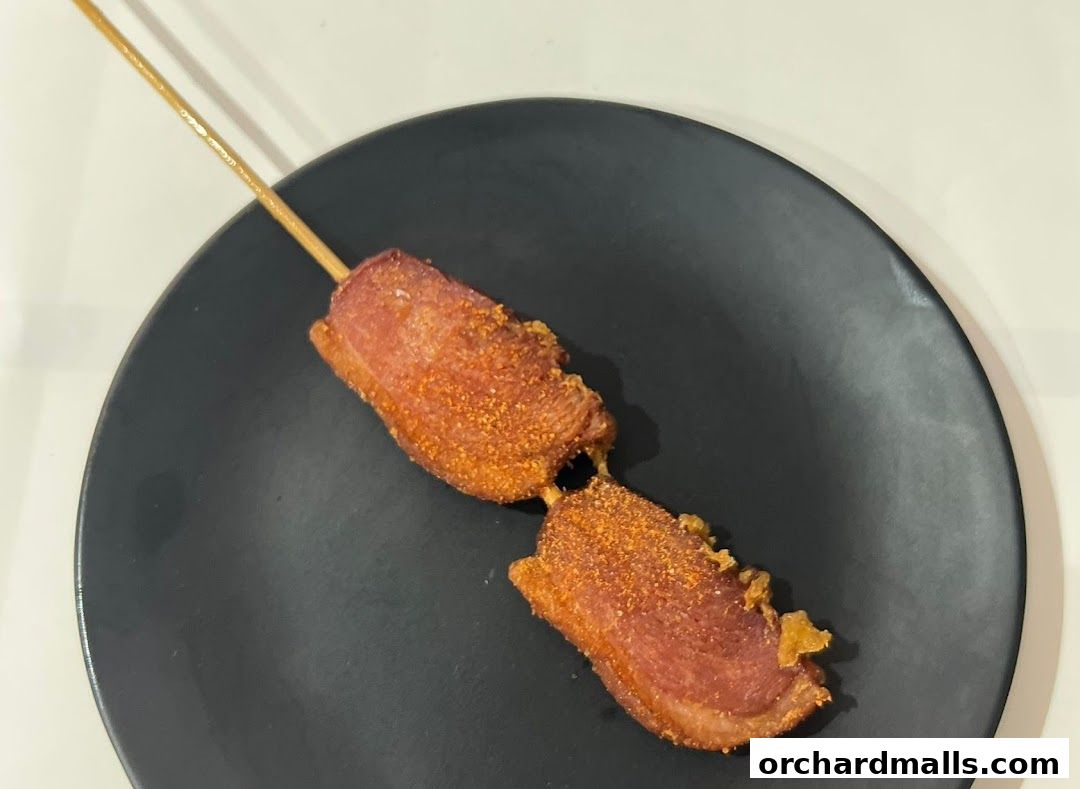 A skewer of fried meat, seasoned with spices, served on a black plate.