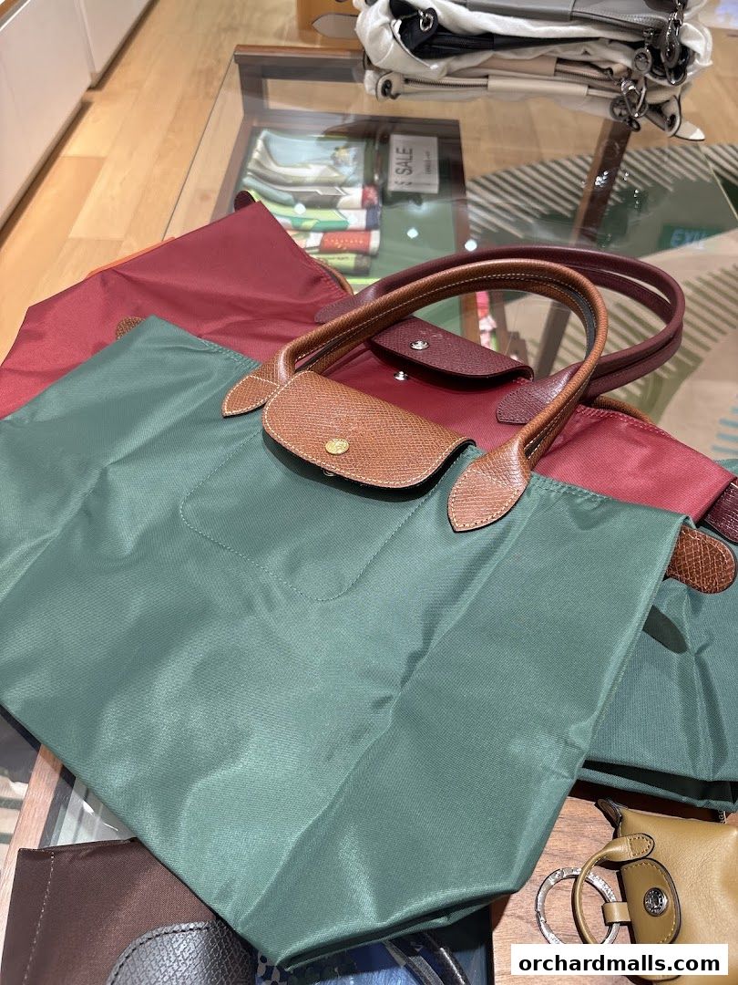 A collection of Longchamp tote bags in various colors, including green and burgundy, displayed on a glass table.